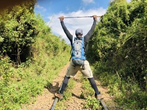 male hiker holding hiking pole over head standing on railway line